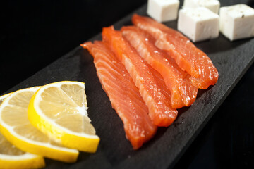 pieces of salmon slice of lemon cream cheese close-up on a black shale board on a black background
