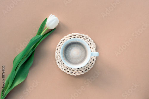 Cup of coffee and white tulip on beige background. Women's day or Mother's day concept. Top view, flat lay, copy space