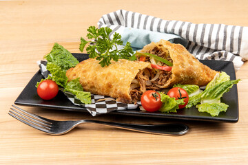 A Brazil or South American pulled pork or pulled chicken filled deep fried pastry (pastel) cut open served on a wooden background