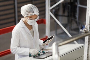 Waist up portrait of female worker pushing buttons on control panel while operating machine units...