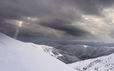 Snow covered slopes under a cloudy sky. The sun's rays pass through the clouds.