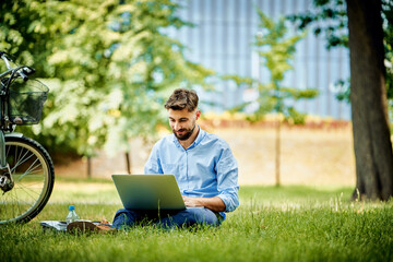 Young business man working on laptop in park - obrazy, fototapety, plakaty