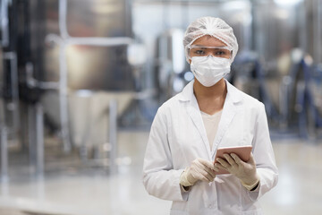 Waist up portrait of young woman working at chemical plant and looking at camera while wearing...
