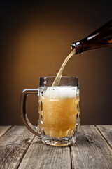 jet beer from bottle to mug on wooden table close-up on warm background