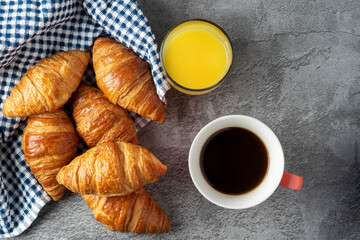 View from above of a cup of coffee and a glass of orange juice next to rich little croissants ready for breakfast. On a gray stone table. Copy space