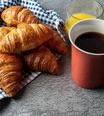 View from above of a cup of coffee and a glass of orange juice next to rich little croissants ready for breakfast. On a gray stone table. 