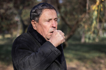 Portrait of a coughing senior man outdoors, looking down. Senior man having sickness, allergies