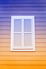 White Louvered Window Shutter on a Purple and Orange Wooden Building