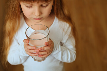 Close-up of strawberry sweet milkshake in the hands of a cute redhead preschool girl. Healthy tasty breakfast for a child