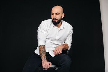 A young bearded man in a white shirt sits on a black background.