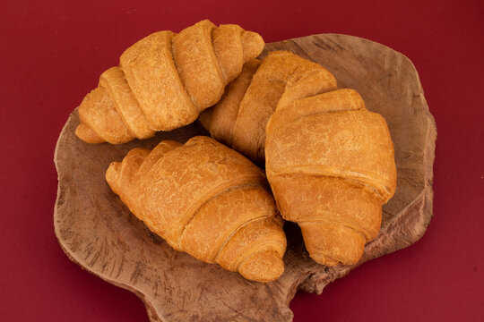 Croissants lie on a wooden stand on a burgundy background
