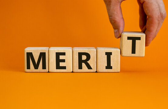 Merit symbol. Wooden cubes with the word 'merit'. Businessman hand. Beautiful orange background, copy space. Business and merit concept.