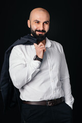 A young bearded man in a white shirt and jacket stands against a black background.
