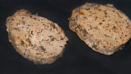 Two pieces of pork loin meat made with spices for loin of daggerboard on black table