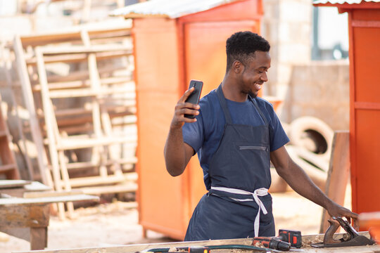 african carpenter smiling while using his phone, like in a video call