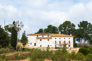 Fototapeta na wymiar Nice Mediterranean country house, quite large, with olive trees and a windmill, on a day with cloudy skies.