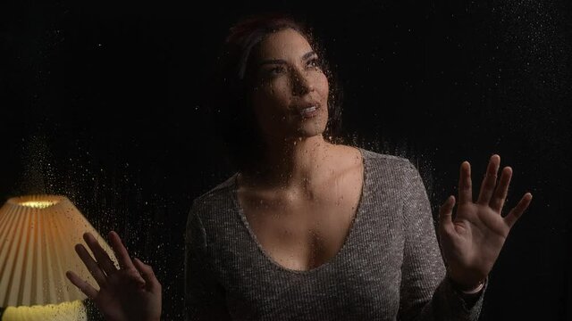 Attractive Latina woman looking out and around at rainy night with her hands on glass. Concerned or wanting look.