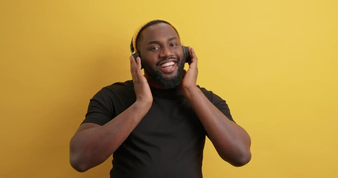 Carefree handsome guy moves slowly with rhythm of music catches every bit of song has happy expression dressed casually uses wireless headphones isolated over yellow background. Check out my moves
