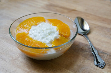 A glass bowl of cottage cheese with sliced peaches on a wood table background with a spoon