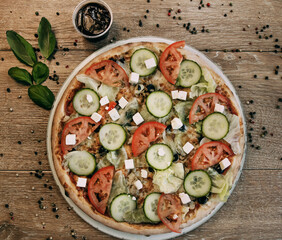 Vegetable pizza with mozzarella, fresh tomatoes and cucumber. Green basil leaves