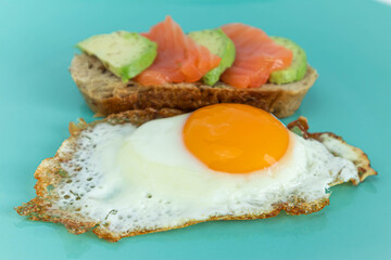 Homemade toast sandwich with salmon and avocado on a slice of cereal bread. Fried eggs with bright yolk on a mint background.