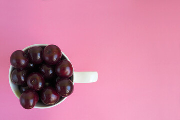 lots of red juicy cherries sprinkled in a white cup on a pink background top view . ripe summer berries