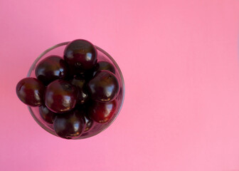 red juicy cherry in a clear glass cup on a pink background top view . ripe summer berries