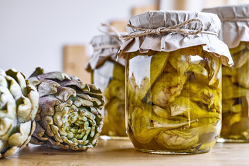 Preserved fermented artichokes in olive oil in glass jars on wooden table. Autumn vegetables...