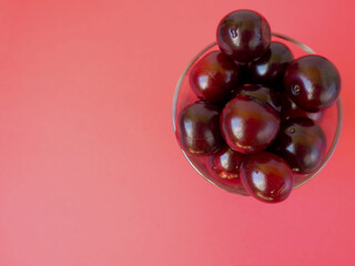 red juicy cherry in a clear glass cup on a red background top view . ripe summer berries