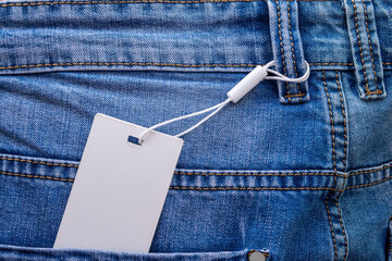 Mockup of a paper blank tag with white cord placed on blue jeans.