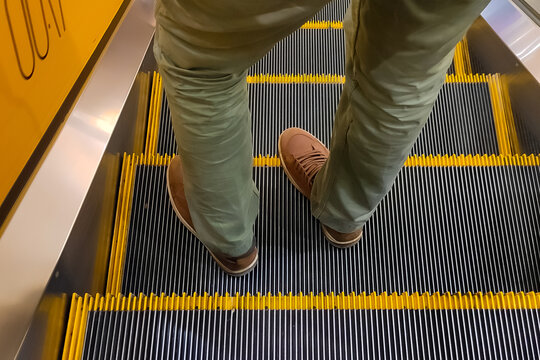 a man stands on an escalator. the legs are in the frame only