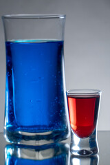 Highball glass filled with aqua and blue dye ink and red shot glass filled with aqua and red dye. Isolated objects in the studio with refelcting surface and gradient background 