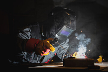 Welder is welding a metal pipes on the workbench in the dark.