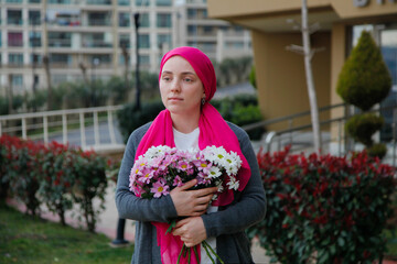 Fototapeta premium Girl in pink scarf and white mask with daisies outdoors. Cancer awareness concept. 