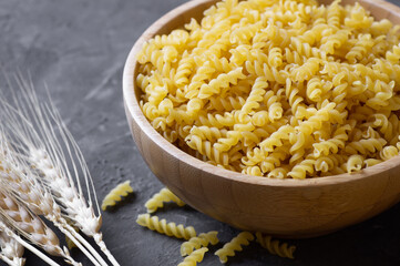 Raw auger pasta in bowl or spoon, uncooked fusilli with wheat