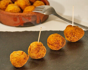 Delcious pincho of 4 round croquettes on a black slate board decorated with croquettes in a bowl of...