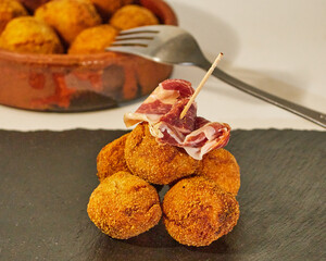 Delcious pincho of several round croquettes with a slice of Iberian Ham on a black slate board...