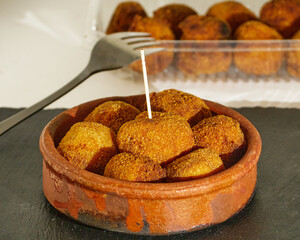 Delicious pincho of several round croquettes in a bowl of mud on a black slate board decorated with croquettes in a plastic box