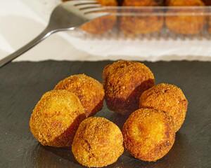 Delicious Pincho of several round croquettes making an horizontal circle on a black slate board decorated with croquettes in a plastic box