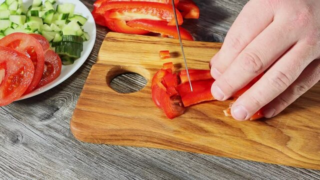 close up view on process of cutting red bell sweet peper with kitchen knife on wooden chopping board