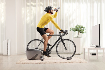Man riding a bike on a trainer and drinking from a bottle at home