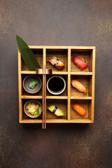 Traditional Japanese sushi in wooden box with soy sauce,wasabi and ginger on brown background.Top view with copy space.