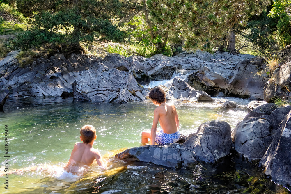 Wall mural two boys on their backs enjoying a swim in a clear mountain river in a rocky, sunlit pool with rocks