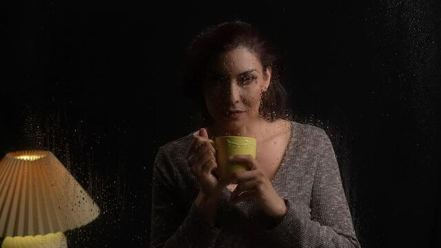 Beautiful Latina woman enjoying coffee looking through window on rainy day with lightning flashes