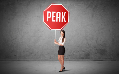 Young business person holding road sign with PEAK inscription, new rules concept