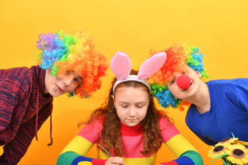 A girl is painting Easter eggs and two clown boys are looking around.