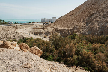 a group of hikers and tourists entering the Nahal Boqeq stream bed nature reserve in Israel with a resort hotel and the Dead Sea in the background