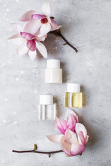 Healthcare cosmetic mockup. White cosmetic bottle containers with pink magnolia flowers on gray background. Natural organic beauty product concept, Minimalism style