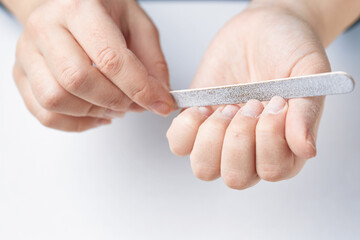 A woman does a manicure at home and uses a nail file to remove old gel polish from her nails....