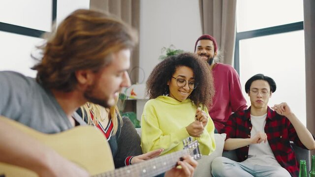 Charismatic company of friends multi ethnic dacing and singing on a guitar in the living room they spend a good time together and enjoying the music